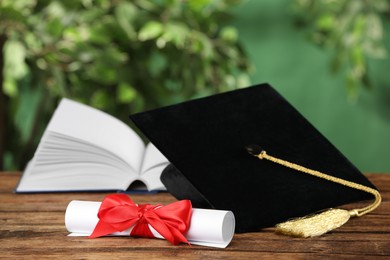 Photo of Graduation hat, book and diploma on wooden table against blurred background