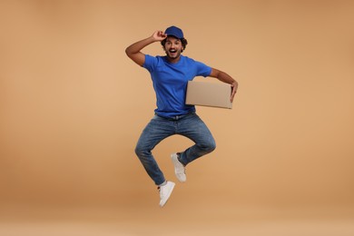 Photo of Happy courier with parcel jumping on light brown background