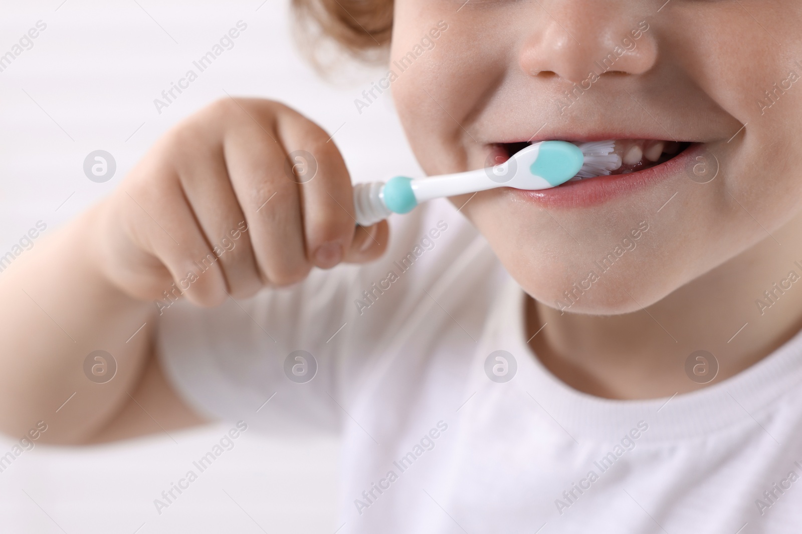 Photo of Little boy brushing his teeth with plastic toothbrush on white background, closeup