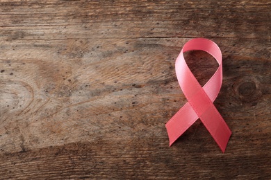 Pink ribbon on wooden background, top view with space for text. Breast cancer awareness concept