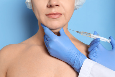 Mature woman with double chin receiving injection on blue background, closeup