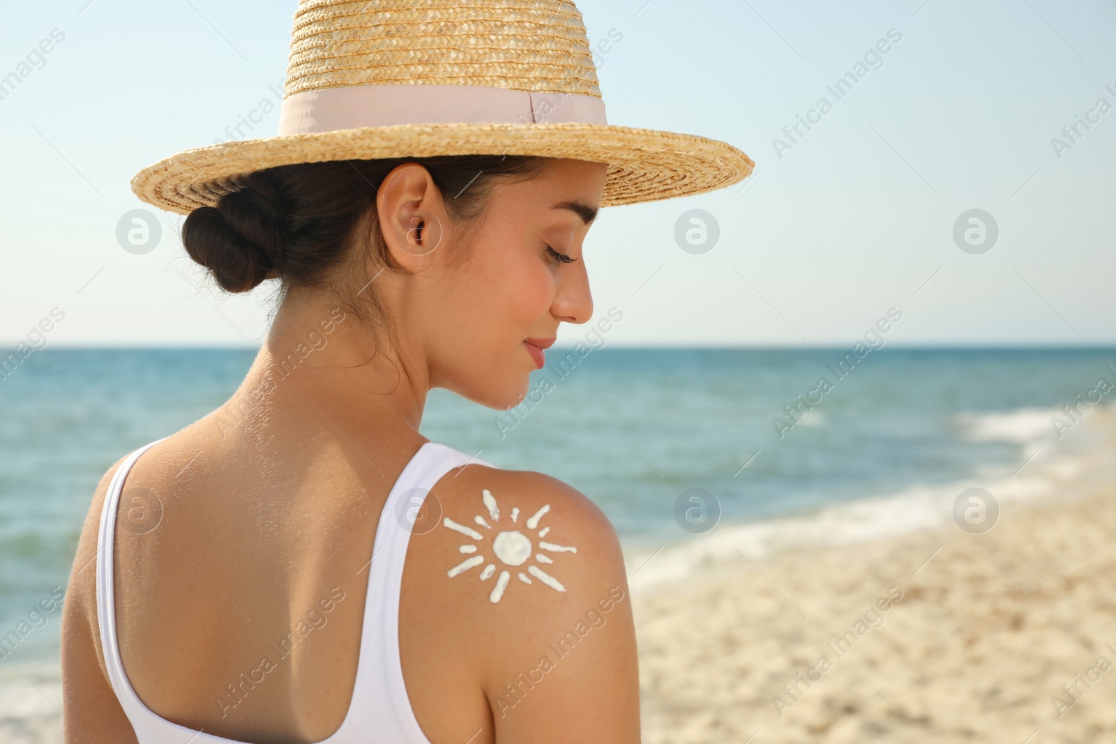 Photo of Beautiful young woman with sun protection cream on shoulder at beach