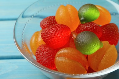 Photo of Delicious gummy fruit shaped candies in glass bowl on light blue table, closeup