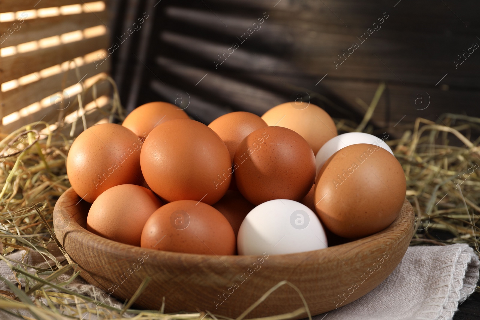 Photo of Fresh chicken eggs in bowl and dried hay on table, closeup