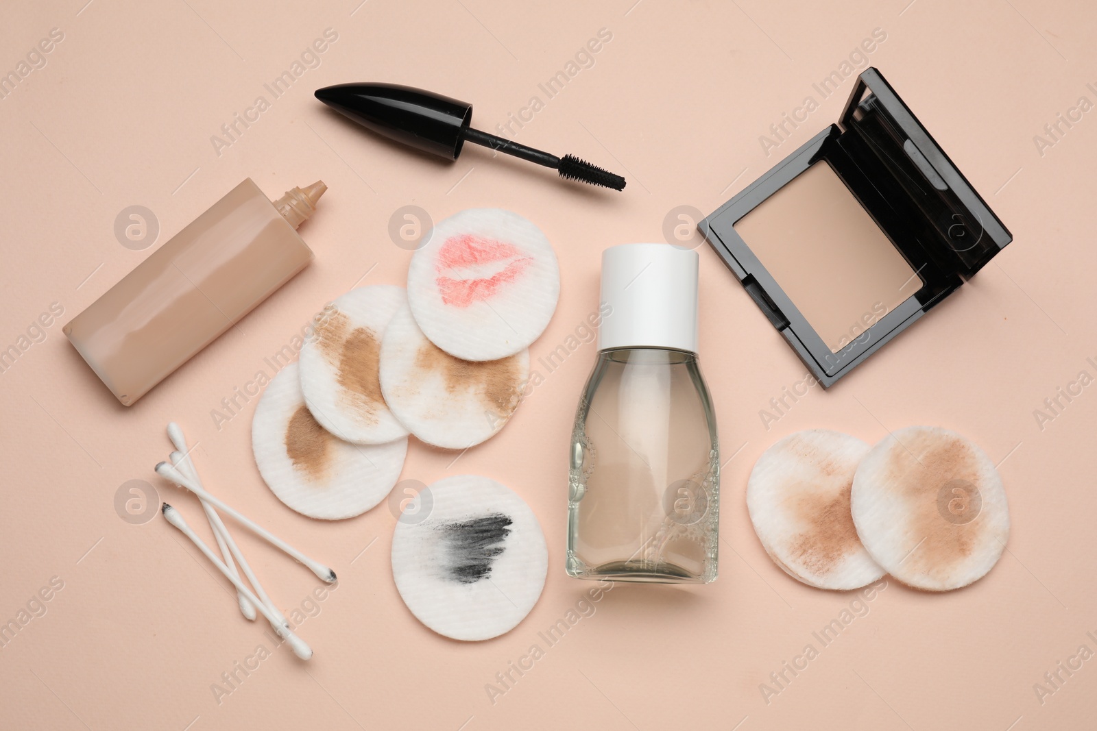 Photo of Bottle of makeup remover, dirty cotton pads, buds and different cosmetic products on beige background, flat lay