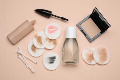 Photo of Bottle of makeup remover, dirty cotton pads, buds and different cosmetic products on beige background, flat lay