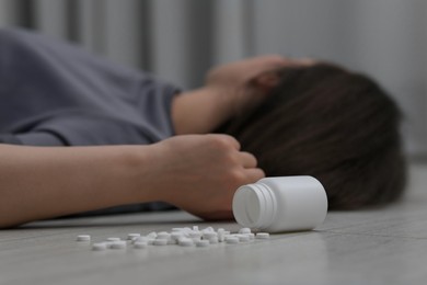 Photo of Woman sleeping near overturned bottle with antidepressants on floor indoors, selective focus