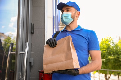 Photo of Courier in protective mask and gloves with order near front door. Restaurant delivery service during coronavirus quarantine