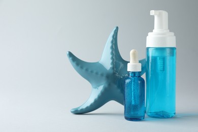 Photo of Bottles of cosmetic products and decorative starfish on light grey background, space for text