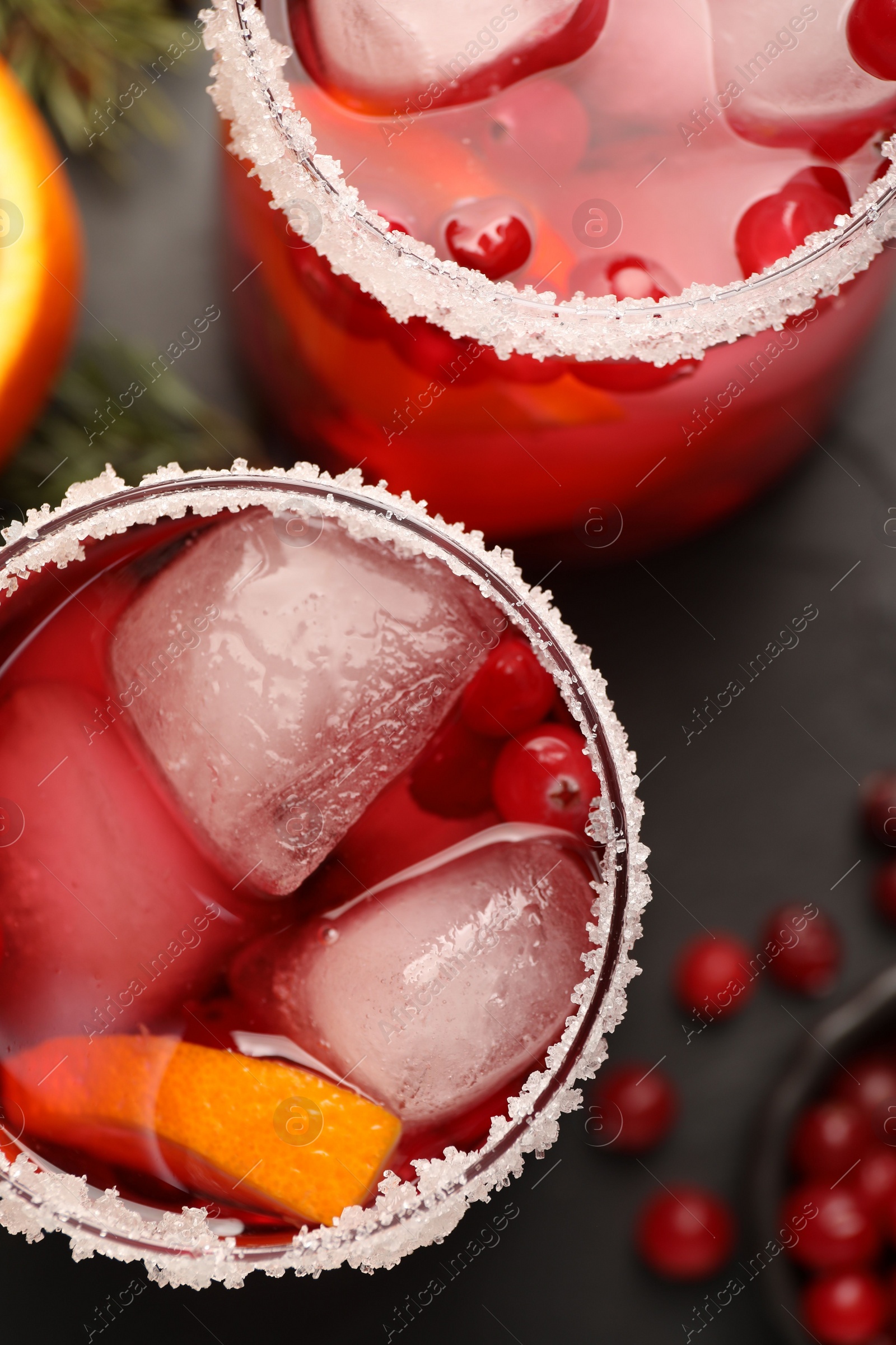 Photo of Tasty cranberry cocktail with ice cubes in glasses on dark gray table, flat lay