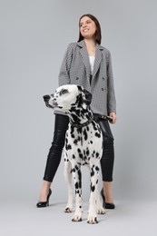 Beautiful young woman with her adorable Dalmatian dog on light grey background. Lovely pet