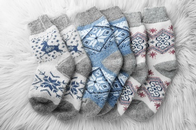 Photo of Knitted socks on white faux fur, flat lay