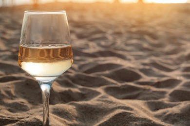 Photo of Glass of tasty wine on sandy beach, space for text