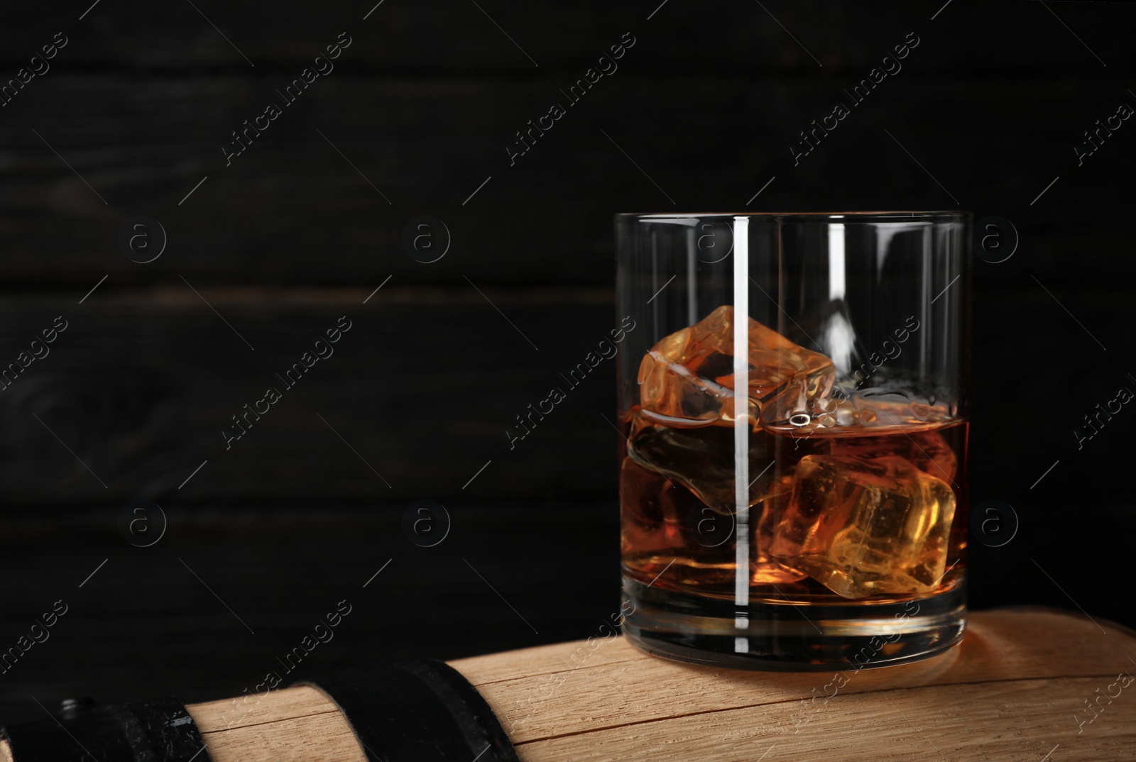 Photo of Golden whiskey in glass with ice cubes on wooden barrel. Space for text
