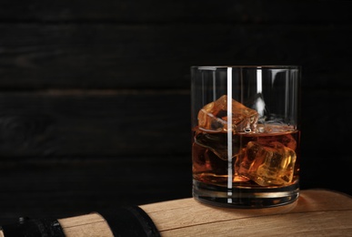 Photo of Golden whiskey in glass with ice cubes on wooden barrel. Space for text