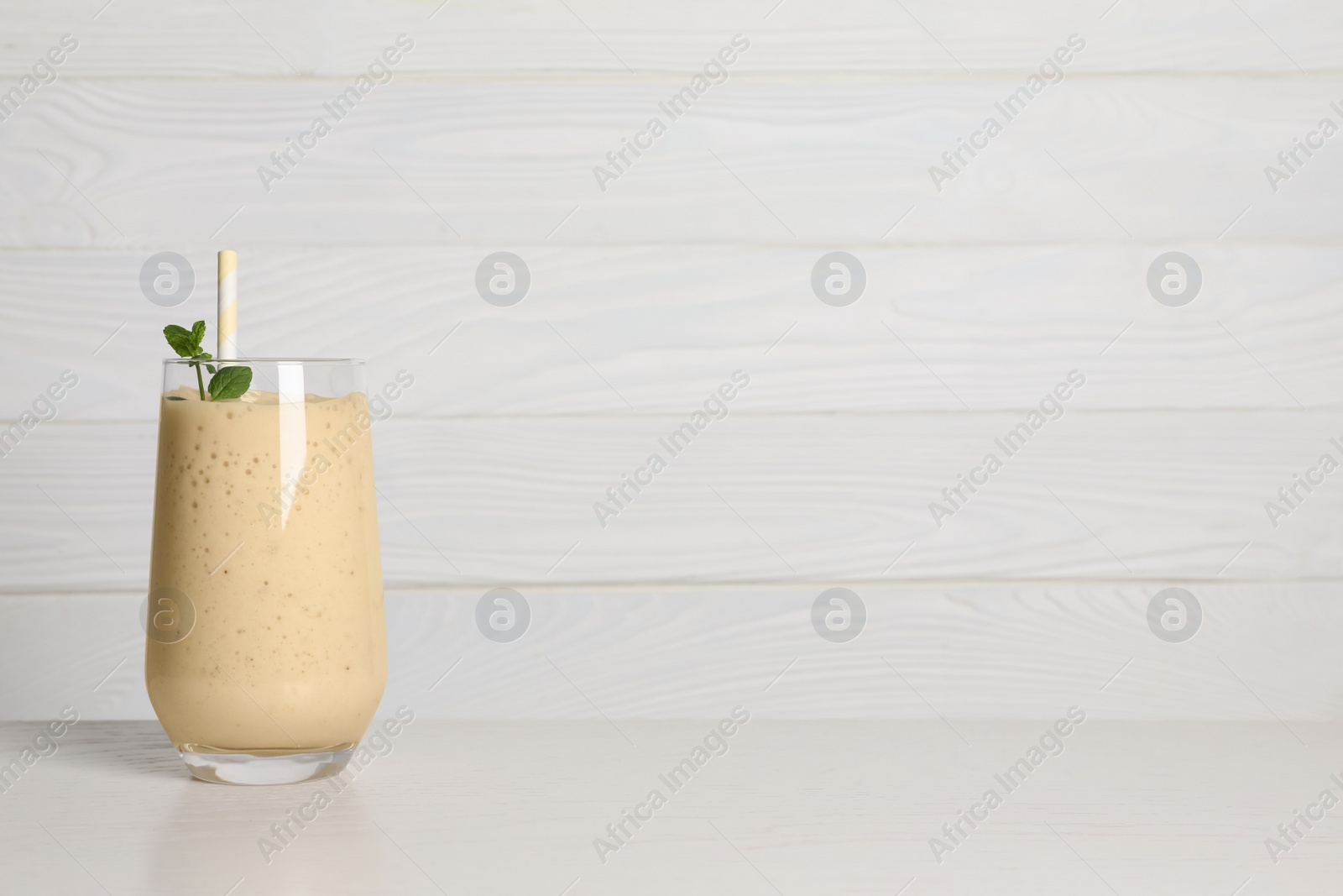 Photo of Glass of tasty smoothie with mint leaves and straw on white wooden table. Space for text