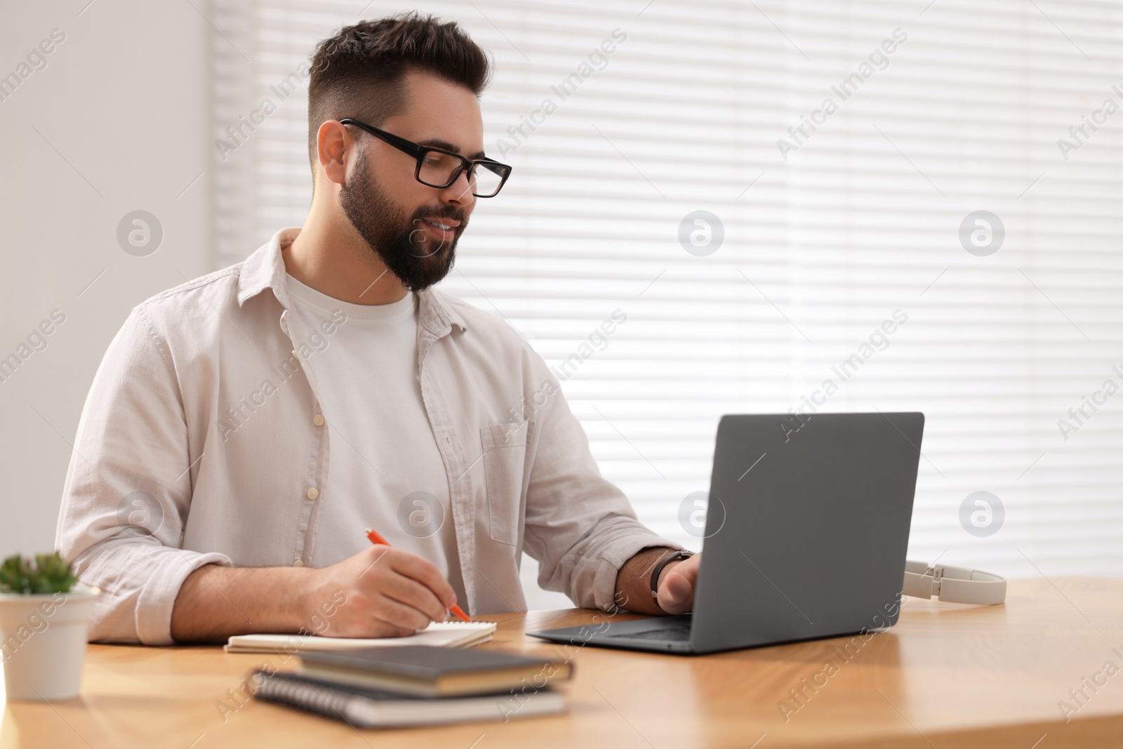 Photo of Young man in glasses watching webinar at table in room