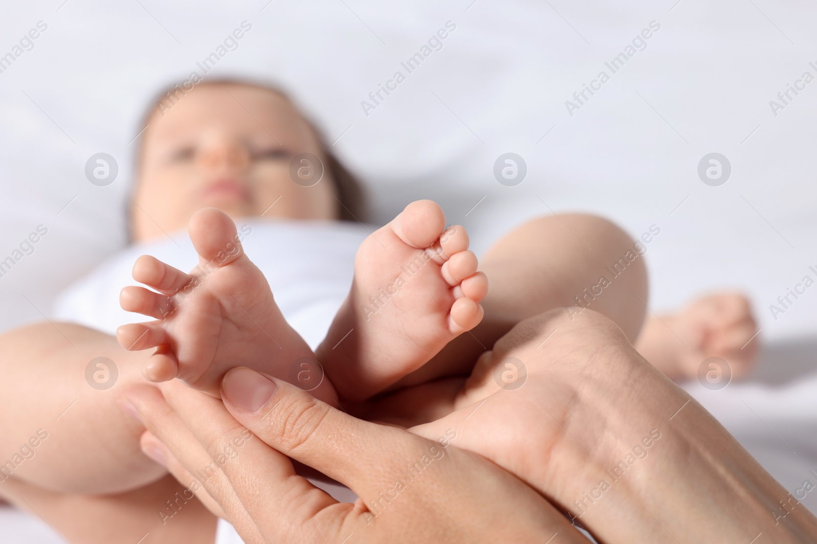 Photo of Mother holding legs of her little baby on bed, closeup