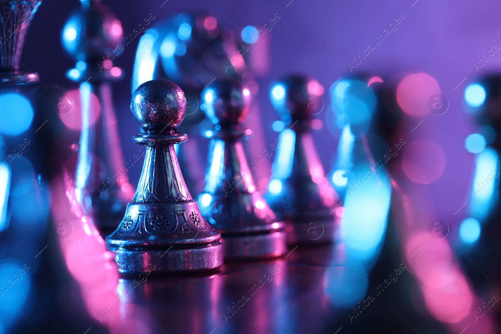 Photo of Chess pawns among other pieces on checkerboard in color light, selective focus