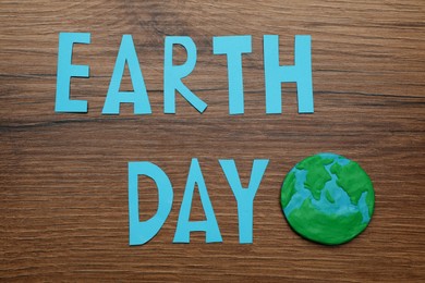 Photo of Words Earth Day and plasticine planet on wooden table, flat lay