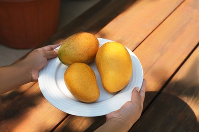 Photo of Woman holding plate with tasty mangoes at wooden table, closeup