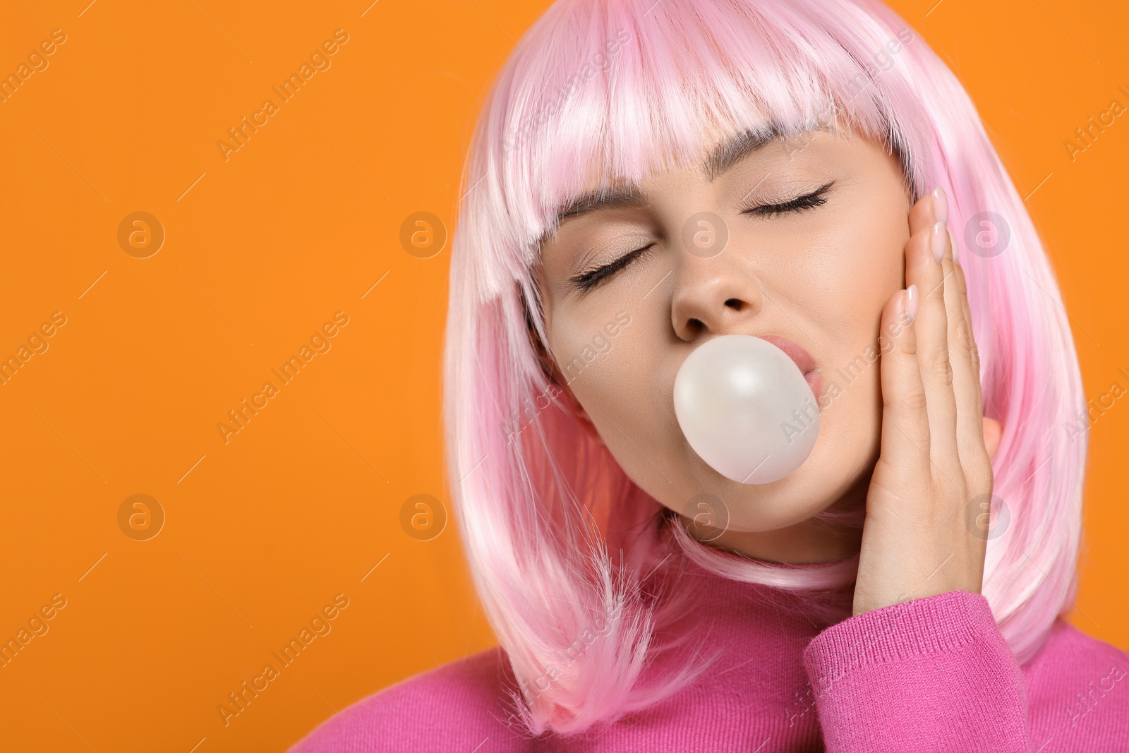 Photo of Beautiful woman blowing bubble gum on orange background, space for text