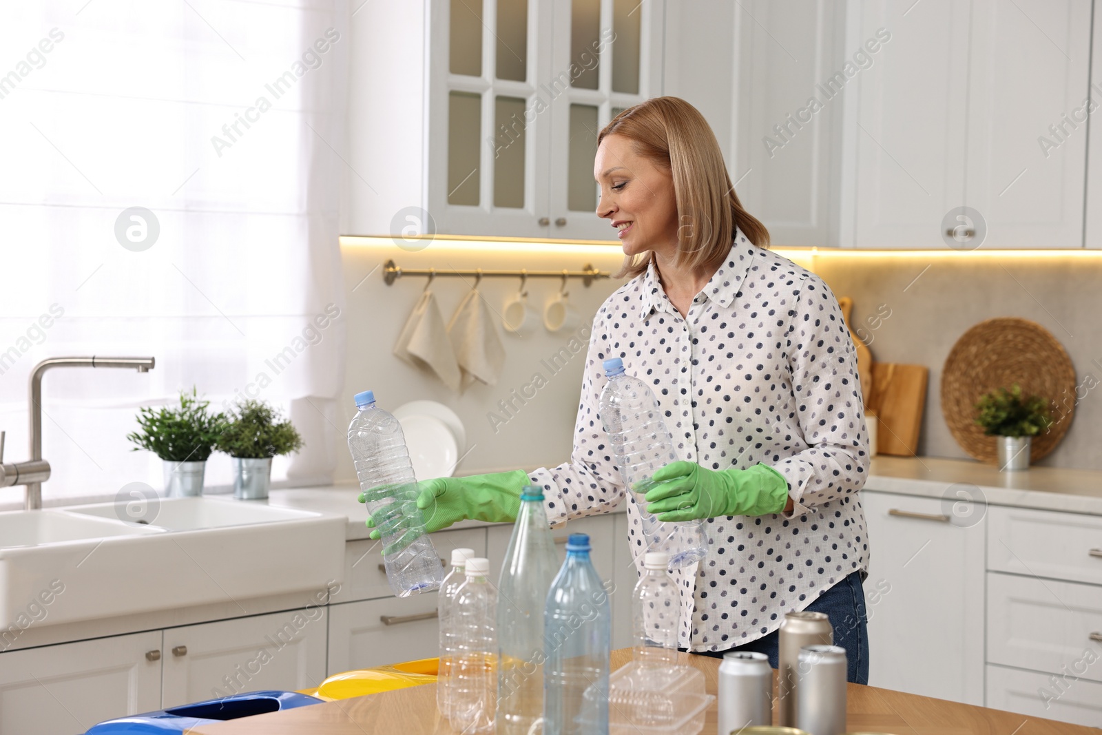 Photo of Smiling woman separating garbage at table in kitchen