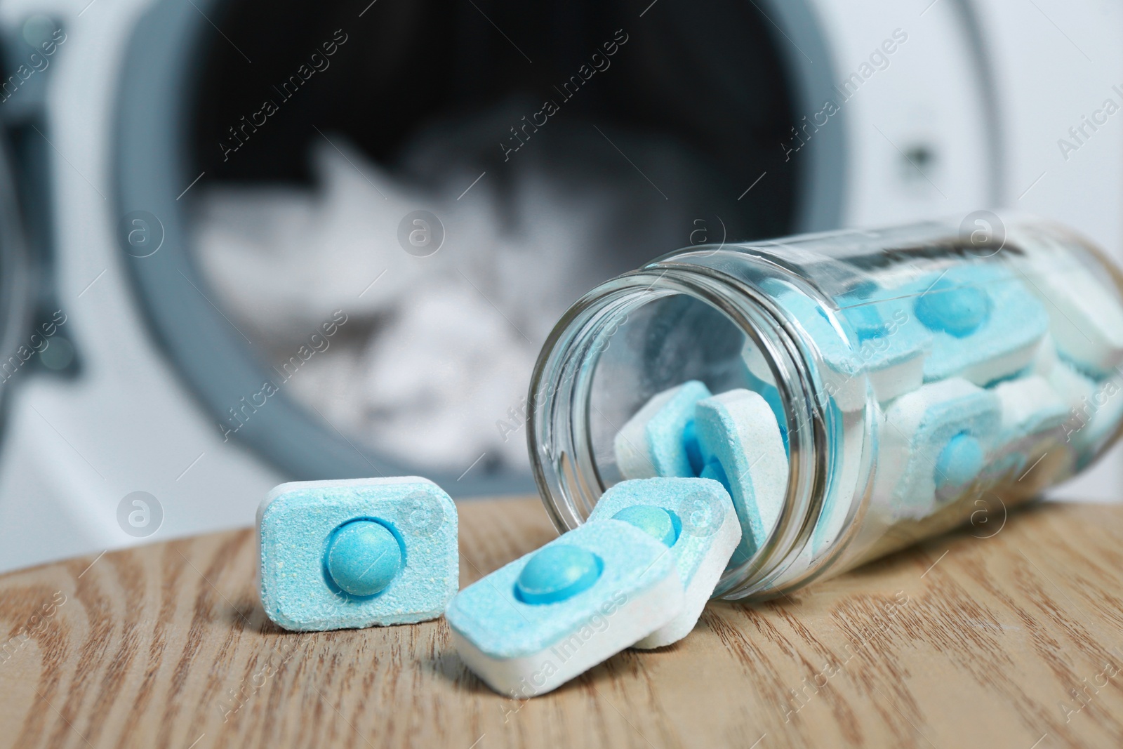 Photo of Jar with water softener tablets on wooden table near washing machine, closeup