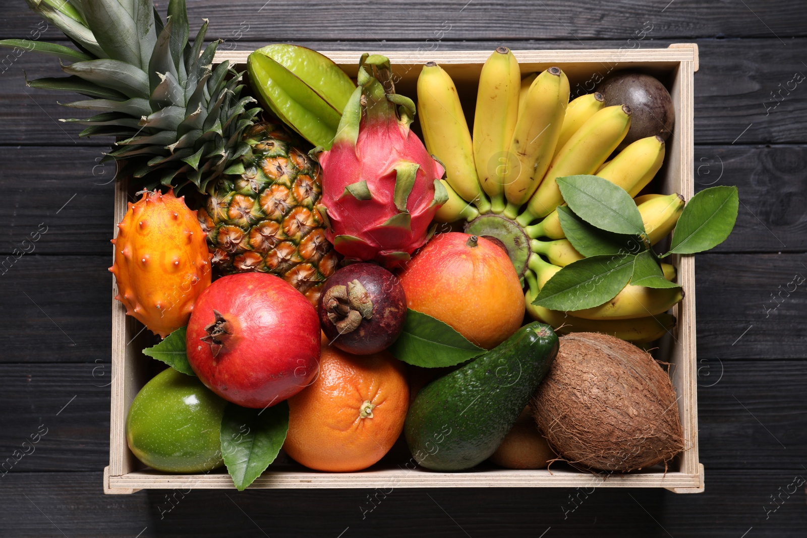 Photo of Crate with different exotic fruits on black wooden table, top view