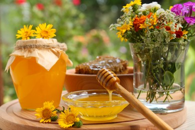 Photo of Delicious honey flowing down from dipper into bowl on wooden table in garden