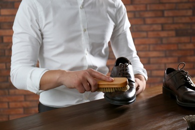 Photo of Man cleaning leather shoe at wooden table indoors, closeup
