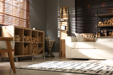 Photo of Shelving unit with stacked firewood and comfortable sofa in stylish room interior
