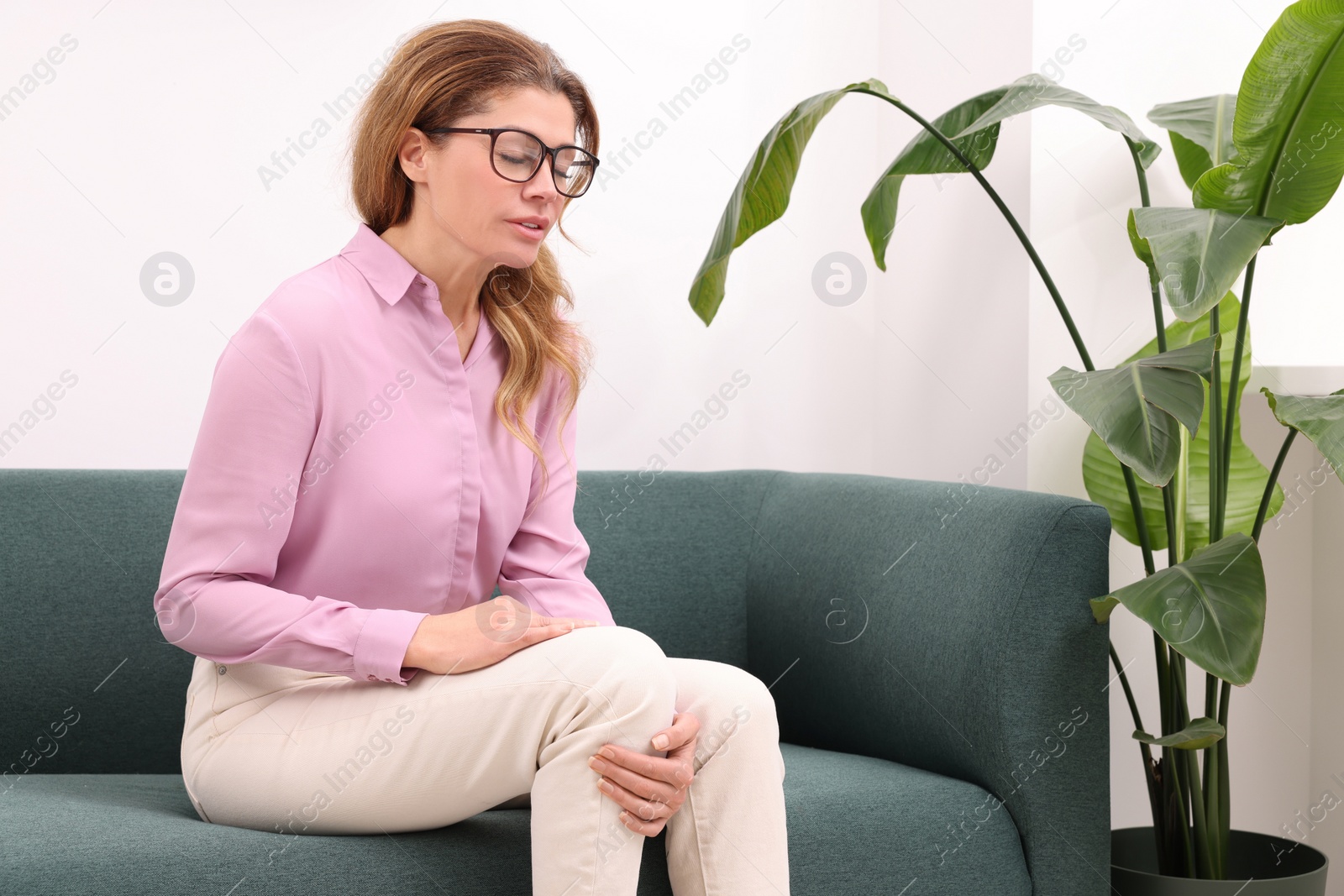 Photo of Woman suffering from knee pain on sofa indoors. Arthritis symptoms