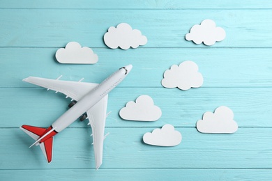 Photo of Toy airplane and clouds on light blue wooden background, flat lay