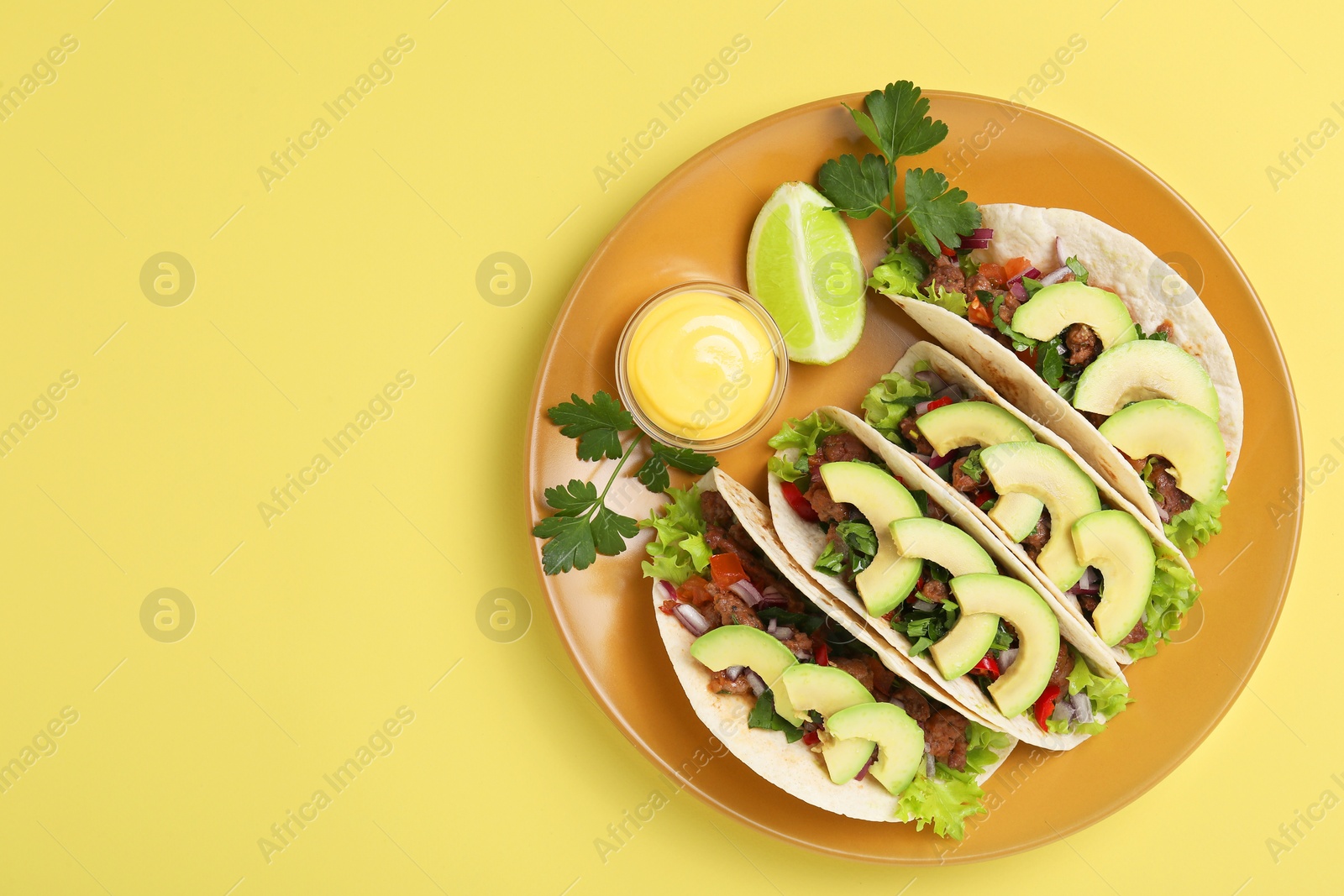 Photo of Delicious tacos with meat, vegetables and avocado served on yellow table, top view. Space for text