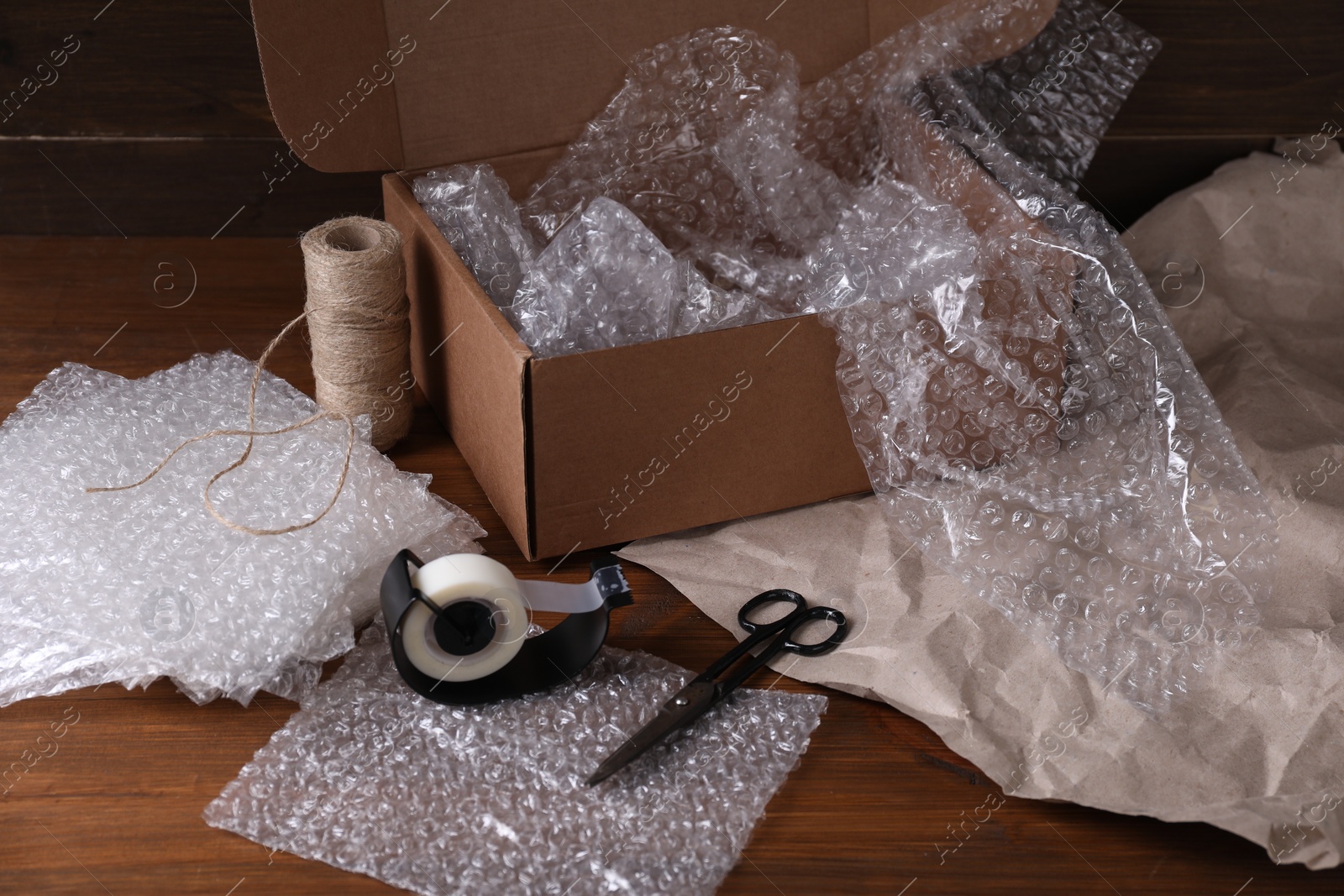 Photo of Bubble wrap, adhesive tape, twine and scissors near cardboard box on wooden table