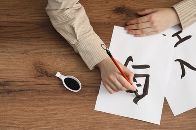 Calligraphy. Woman with brush and inkwell writing hieroglyphs on paper at wooden table, top view