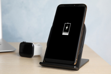 Photo of Mobile phone charging with wireless pad on wooden table, closeup