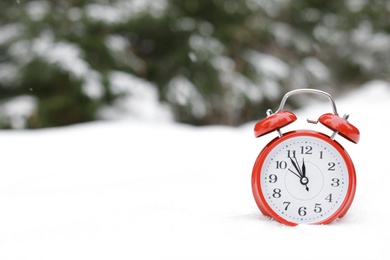 Photo of Red alarm clock on white snow outdoors. Space for text