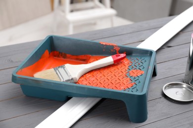 Photo of Tray with orange paint and brush on grey wooden table indoors