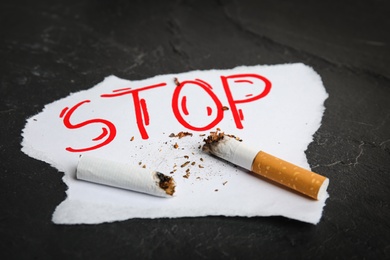 Photo of Cigarette stubs and paper with word Stop on black table. Quitting smoking concept
