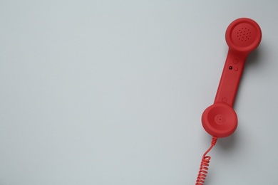 Photo of Red corded telephone handset on light grey background, top view. Hotline concept