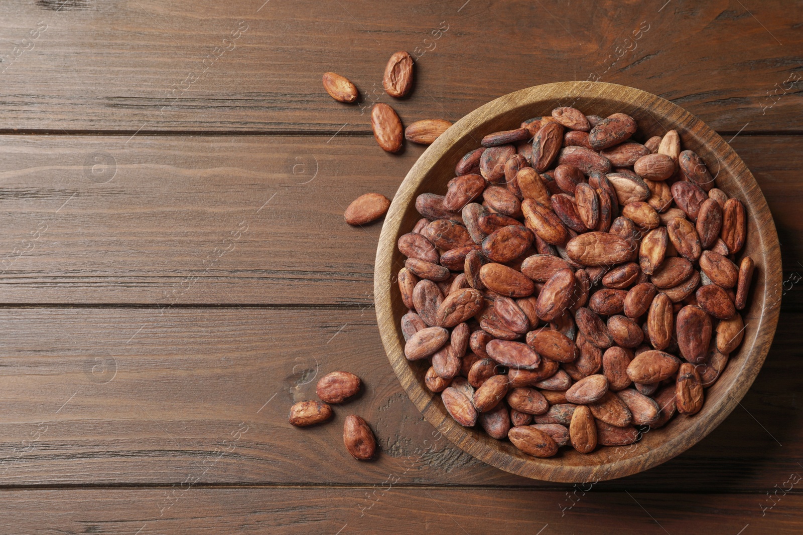 Photo of Bowl with cocoa beans on wooden table, top view. Space for text