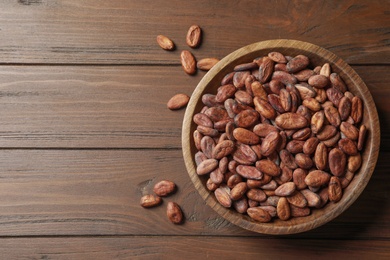 Photo of Bowl with cocoa beans on wooden table, top view. Space for text