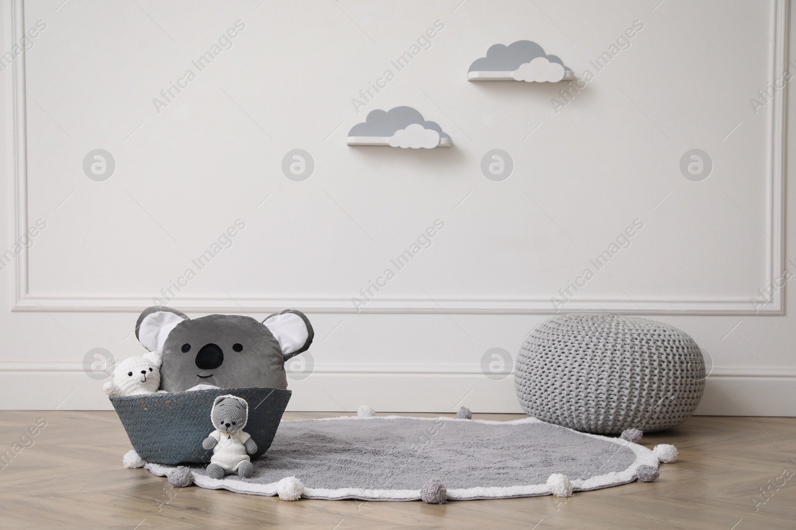 Photo of Wicker basket, toys and pouf near white wall indoors. Interior design