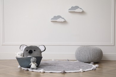 Wicker basket, toys and pouf near white wall indoors. Interior design