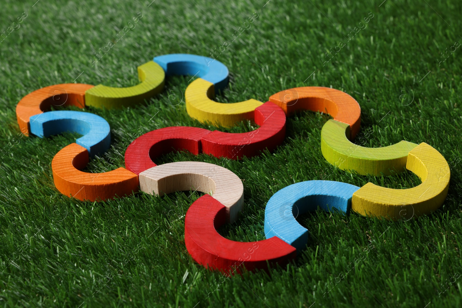 Photo of Colorful wooden pieces of play set on green grass, closeup. Educational toy for motor skills development