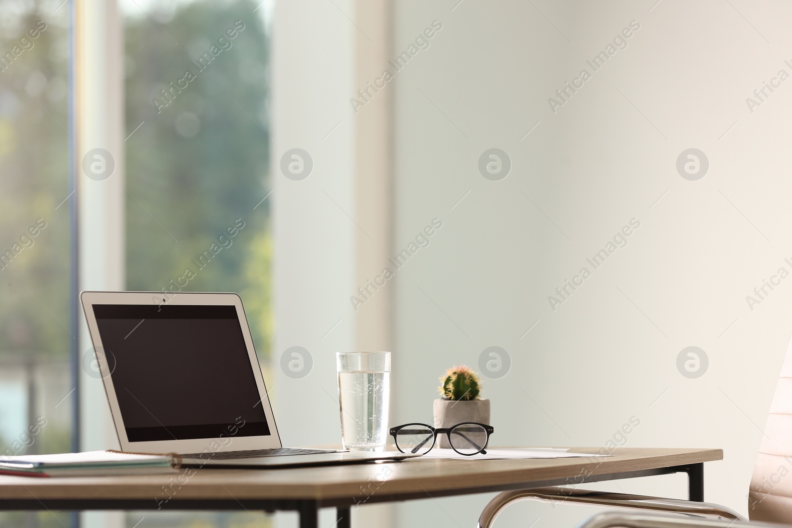 Photo of Modern laptop and glass of water on table in office. Space for text