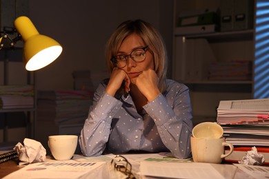 Photo of Woman snoozing at table in office at night. Overwhelmed by work