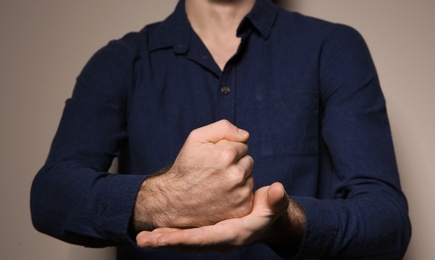 Photo of Man showing word CRUCIFY in sign language on color background, closeup